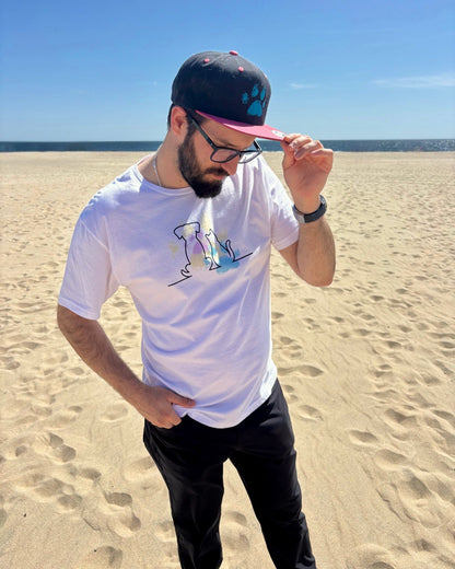 man on the beach, with the ocean in the background. Showcasing his black and pink hat with a blue dog paw print on it. 
